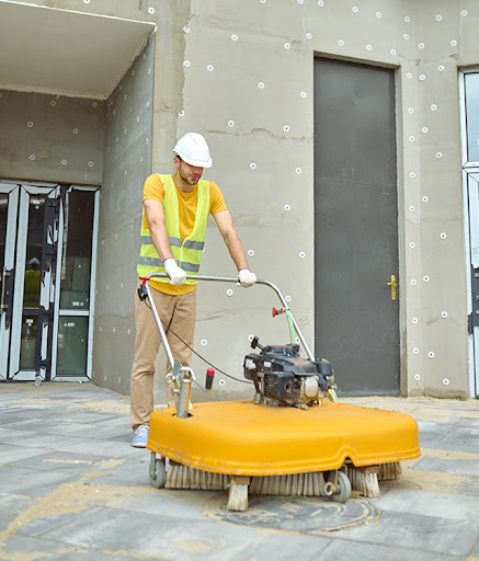 Cleaner scrubbing warehouse floor near pallet racks and loading area